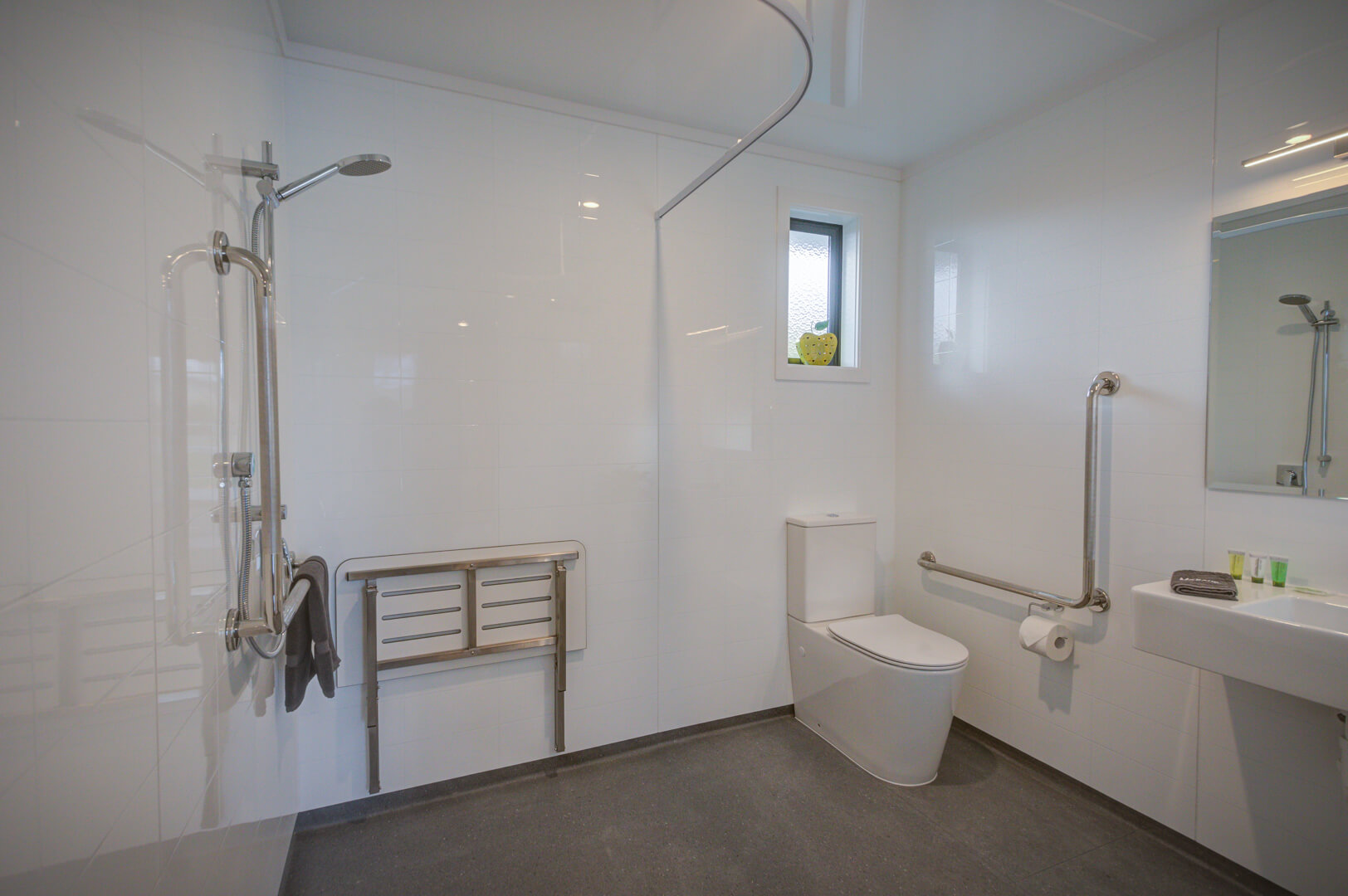 Spacious accessible bathroom with toilet and open-tiled shower 