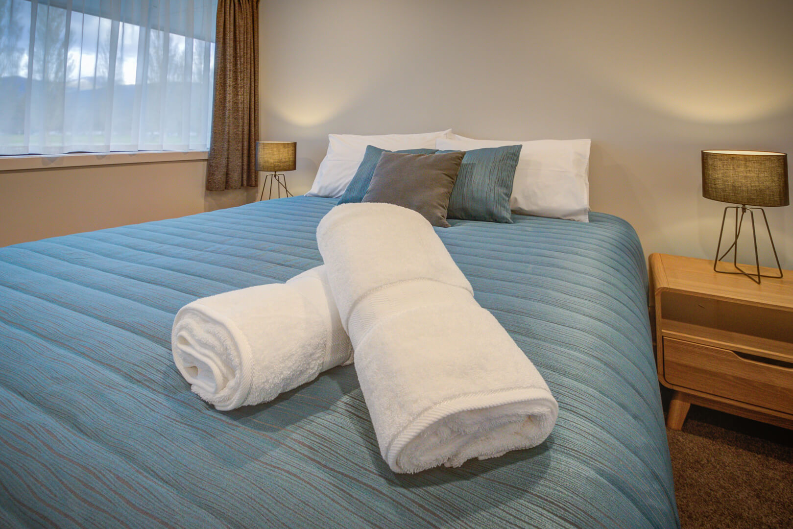 King sized bed with blue bed covers flanked by bedside tables and lamps atop.